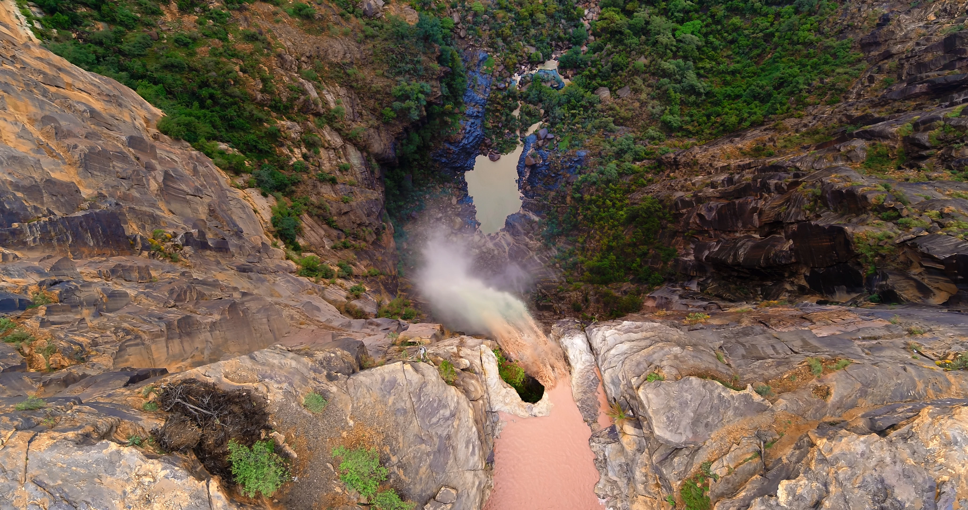 Dramatic bird's eye view of waterfall and sheer rocky drop to the floor of Wadi Lajab canyon in Zahwan Mountain in Jazan